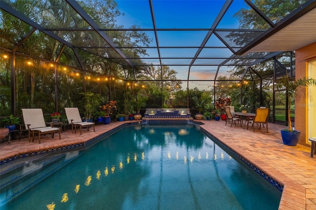 pool at dusk featuring an outdoor pool, glass enclosure, and a patio area