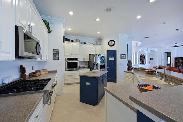 kitchen featuring white cabinets, dark countertops, a center island, stainless steel appliances, and a sink