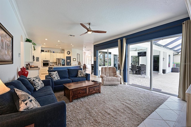 living room with a textured ceiling, ceiling fan, light tile patterned flooring, visible vents, and ornamental molding