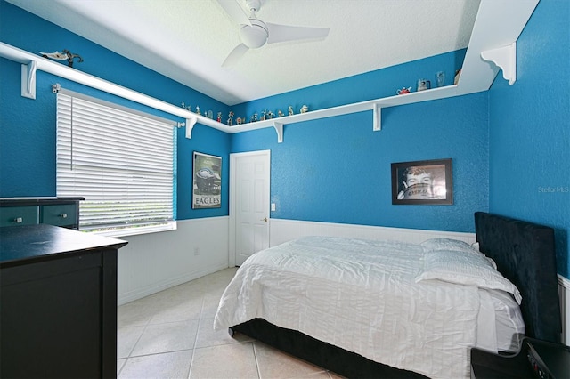 bedroom with a ceiling fan, wainscoting, a textured ceiling, and light tile patterned floors