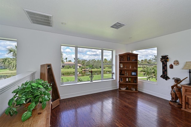 interior space with a water view, baseboards, visible vents, and dark wood finished floors