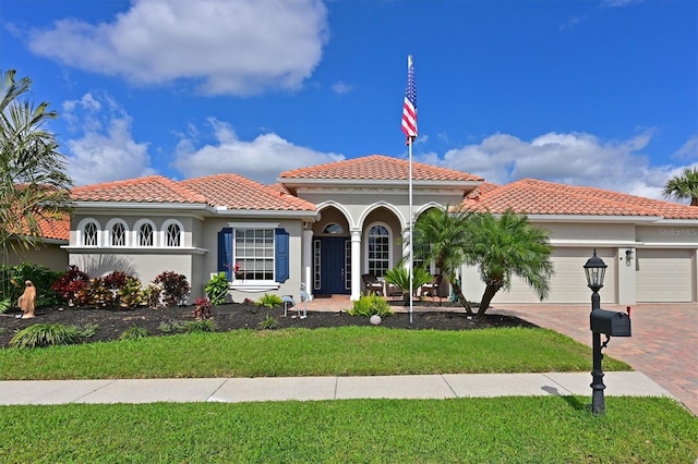 mediterranean / spanish house with a garage, a tile roof, decorative driveway, a front lawn, and stucco siding