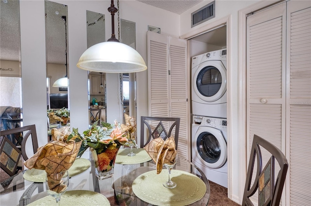 clothes washing area featuring a textured ceiling, laundry area, visible vents, and stacked washer / drying machine