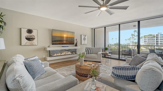 living area with ceiling fan, floor to ceiling windows, wood finished floors, and a glass covered fireplace