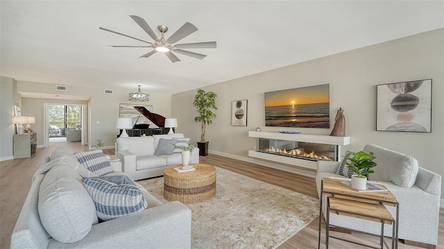 living area with a glass covered fireplace, baseboards, visible vents, and light wood finished floors