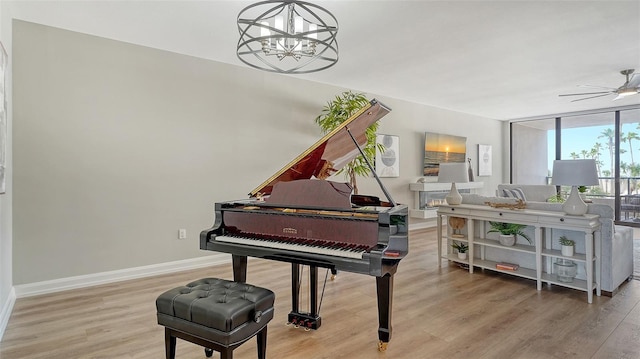 sitting room with ceiling fan with notable chandelier, light wood finished floors, and baseboards