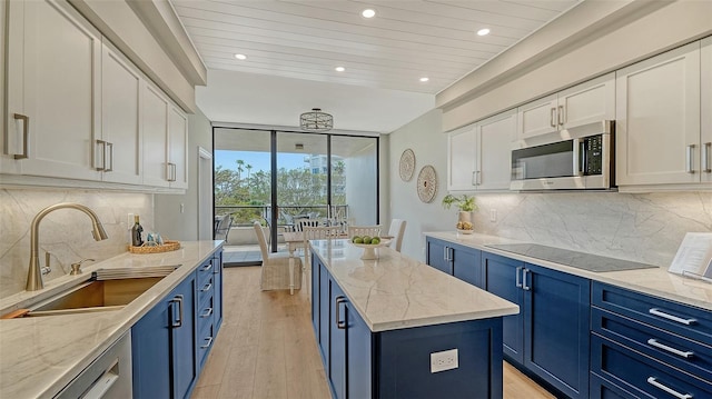 kitchen with black electric stovetop, blue cabinets, a sink, floor to ceiling windows, and stainless steel microwave