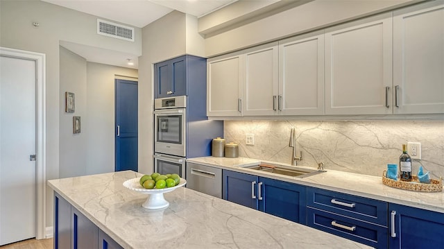 kitchen with blue cabinets, stainless steel appliances, a sink, visible vents, and backsplash