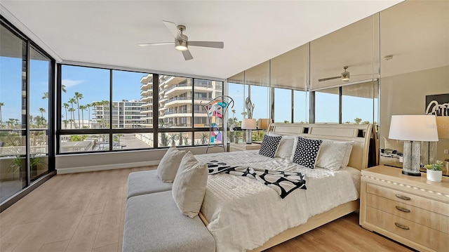 bedroom featuring light wood finished floors, a ceiling fan, a city view, and a sunroom