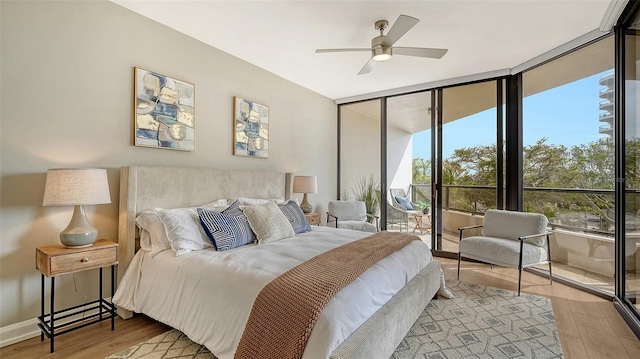 bedroom featuring a ceiling fan, wood finished floors, a wall of windows, access to outside, and baseboards