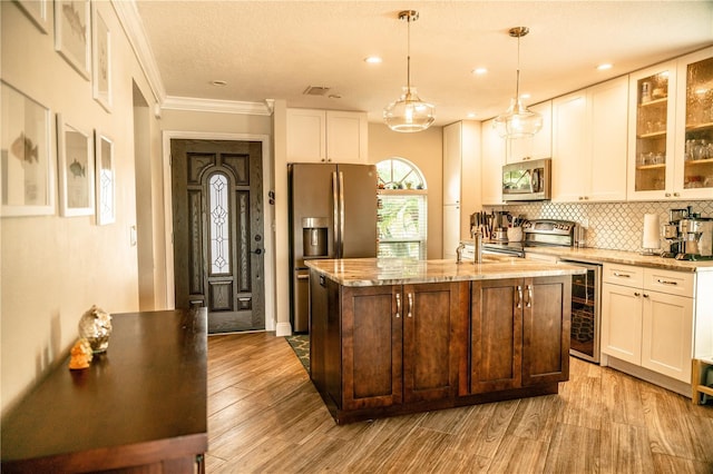 kitchen featuring wine cooler, wood finished floors, appliances with stainless steel finishes, decorative backsplash, and an island with sink