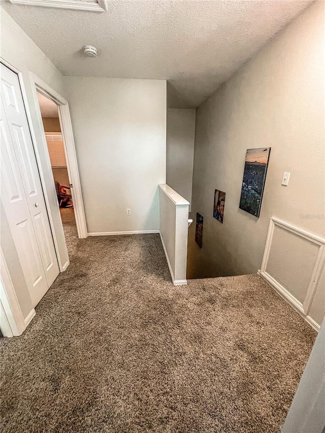 hall with carpet flooring, a textured ceiling, and baseboards