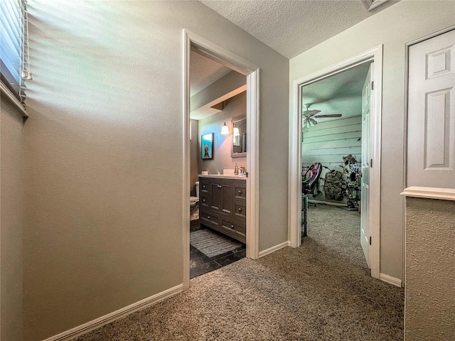 hallway with carpet floors, baseboards, and a textured ceiling