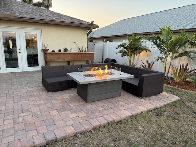 patio terrace at dusk with an outdoor living space with a fire pit, french doors, and fence