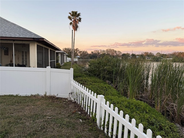 yard at dusk featuring a sunroom and fence