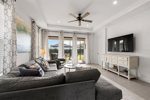 living room featuring a tray ceiling, ceiling fan, and light tile patterned floors
