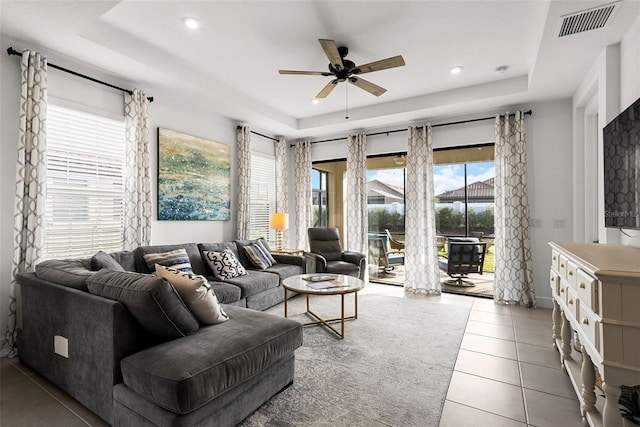 living room with tile patterned floors, a tray ceiling, and ceiling fan