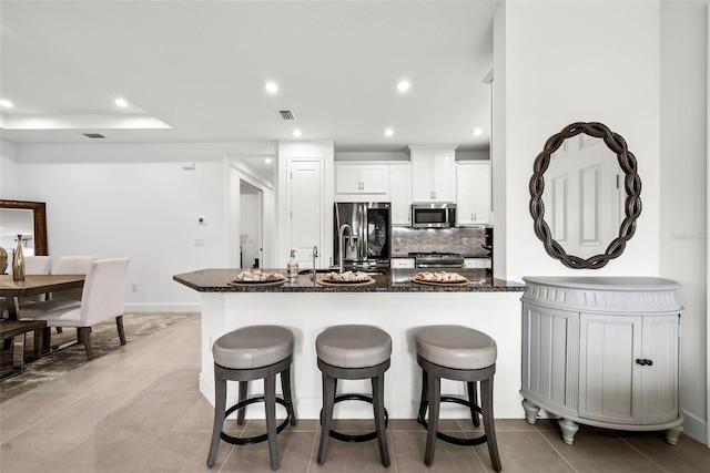 kitchen featuring white cabinetry, dark stone countertops, stainless steel appliances, and a kitchen breakfast bar