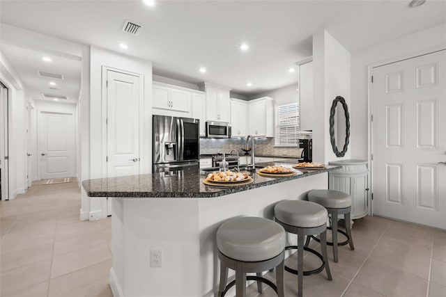 kitchen featuring white cabinetry, stainless steel appliances, dark stone counters, and light tile patterned floors
