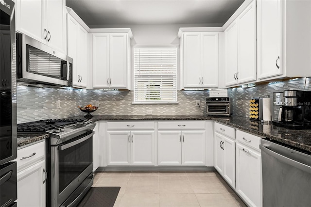 kitchen featuring appliances with stainless steel finishes, tasteful backsplash, dark stone counters, light tile patterned floors, and white cabinetry