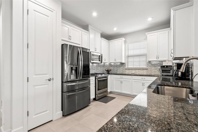 kitchen featuring stainless steel appliances, backsplash, sink, white cabinetry, and dark stone countertops