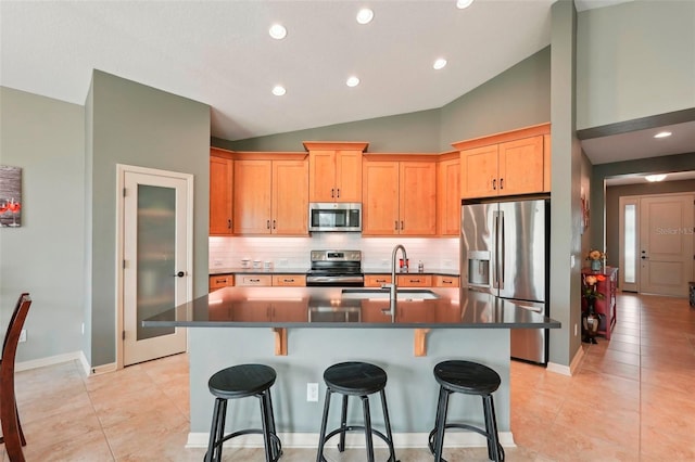 kitchen featuring dark countertops, a kitchen island with sink, stainless steel appliances, and a sink