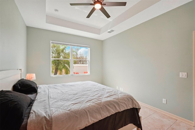 bedroom featuring visible vents, baseboards, a ceiling fan, a tray ceiling, and light tile patterned flooring