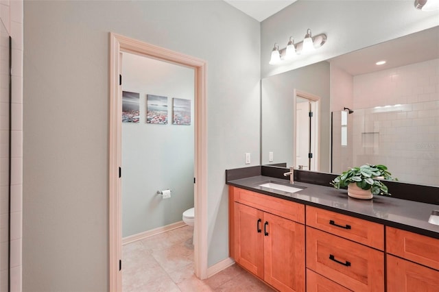 bathroom with toilet, vanity, baseboards, a tile shower, and tile patterned floors