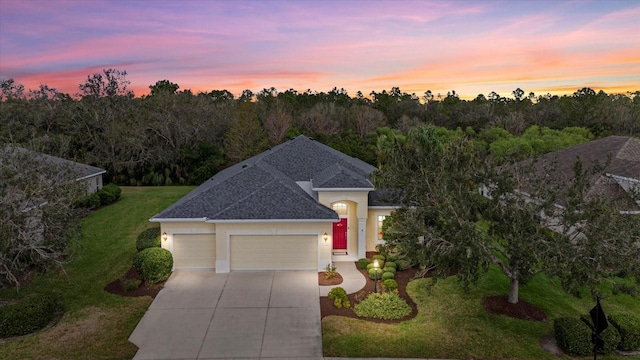 view of front of home featuring stucco siding, a shingled roof, a garage, driveway, and a front lawn