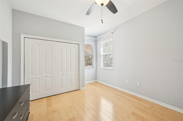 unfurnished bedroom with light wood-type flooring, a ceiling fan, baseboards, and a closet