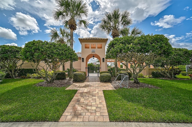 view of front facade with a tile roof, a gate, a front lawn, and stucco siding