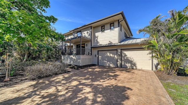 view of front of property featuring a balcony, metal roof, an attached garage, a standing seam roof, and decorative driveway