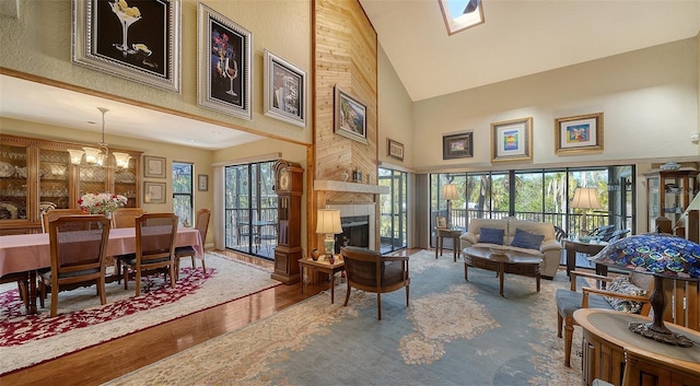 living area with high vaulted ceiling, a notable chandelier, a skylight, a fireplace, and wood finished floors