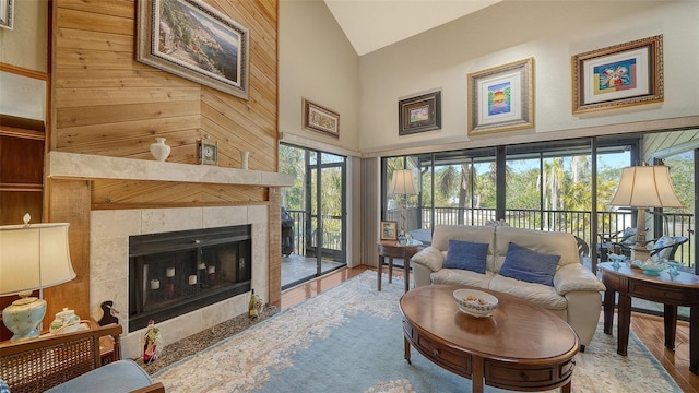 living area with high vaulted ceiling, a tile fireplace, and wood finished floors