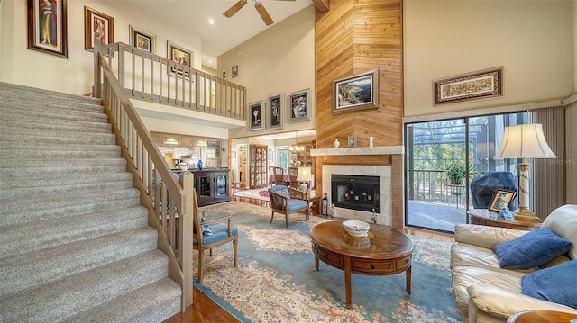 living area with stairs, a high ceiling, a ceiling fan, and a tile fireplace