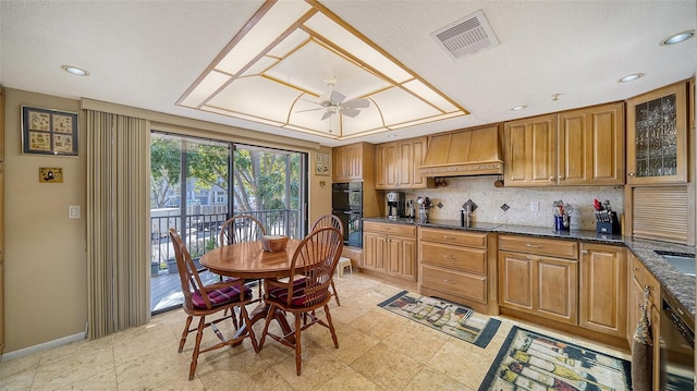 kitchen with visible vents, glass insert cabinets, brown cabinetry, dark stone countertops, and premium range hood