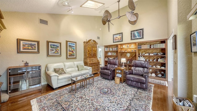 living area with high vaulted ceiling, a skylight, wood finished floors, and visible vents