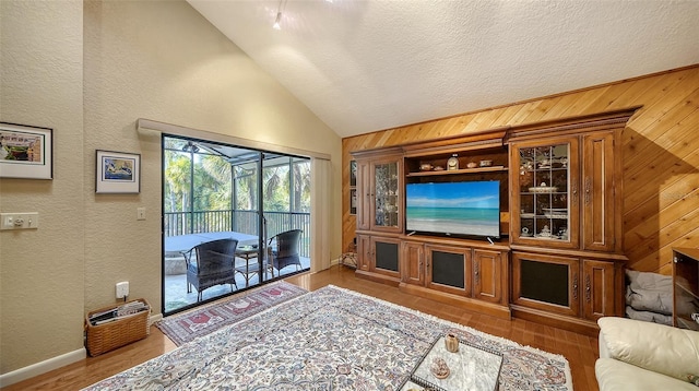 living area featuring vaulted ceiling, a textured wall, wood finished floors, and wooden walls