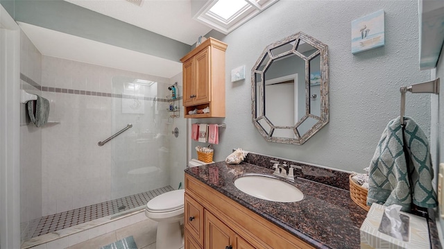 bathroom with a skylight, a textured wall, toilet, vanity, and tiled shower