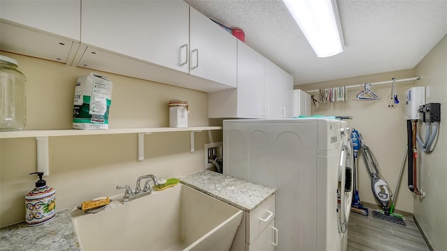 clothes washing area featuring cabinet space, a sink, a textured ceiling, light wood-type flooring, and independent washer and dryer