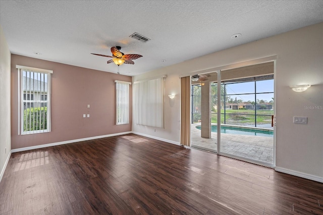 empty room with plenty of natural light, a textured ceiling, visible vents, and wood finished floors