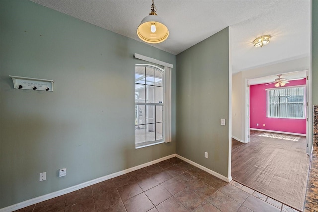 unfurnished room with a textured ceiling, ceiling fan, tile patterned flooring, and baseboards