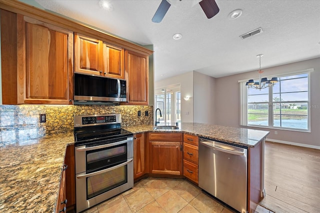 kitchen featuring a peninsula, appliances with stainless steel finishes, brown cabinets, and a sink