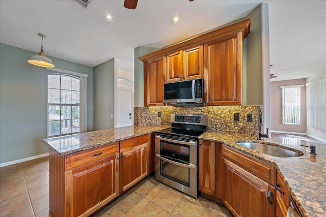 kitchen with stainless steel appliances, tasteful backsplash, brown cabinetry, a sink, and a peninsula