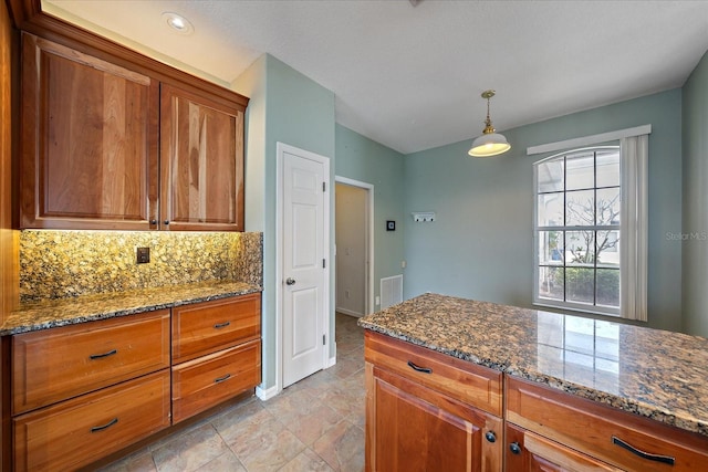 kitchen featuring tasteful backsplash, dark stone counters, and brown cabinetry