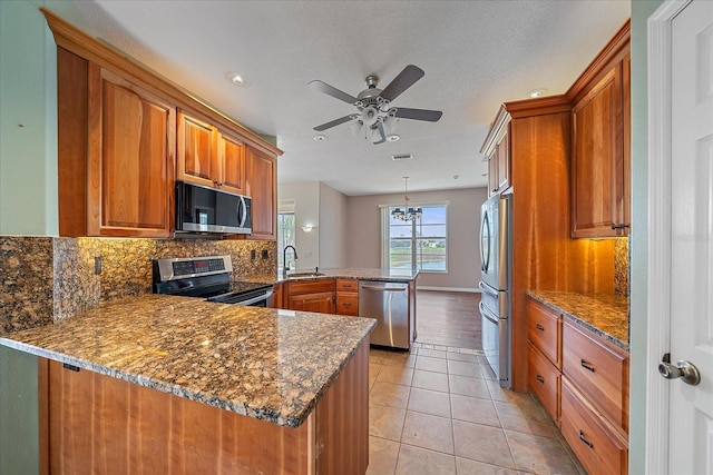 kitchen with appliances with stainless steel finishes, brown cabinetry, a peninsula, and light tile patterned flooring