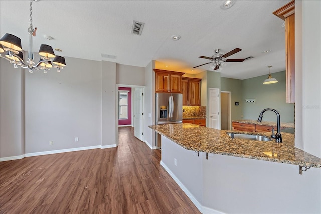 kitchen with a peninsula, a sink, visible vents, dark stone counters, and brown cabinetry