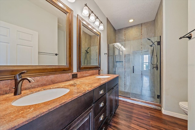 full bath with double vanity, toilet, wood finished floors, a shower stall, and a sink