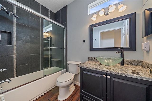 full bath featuring shower / bath combination with glass door, toilet, a textured ceiling, vanity, and wood finished floors