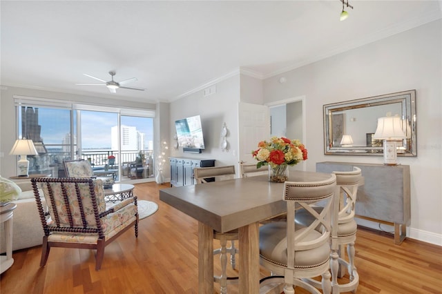 dining room featuring ceiling fan, visible vents, baseboards, ornamental molding, and light wood finished floors